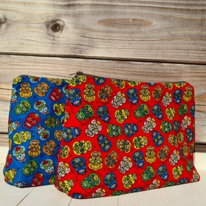Op de afbeelding: Twee ritsen met een kleurrijk schedelpatroon. De tas aan de linkerkant is blauw met witte schedels en de tas aan de rechterkant is rood met witte, blauwe en gele schedels.