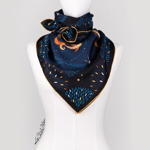 Puede incluir: Un pa&ntilde;uelo cuadrado de seda con fondo azul marino y borde dorado. El pa&ntilde;uelo presenta un dise&ntilde;o caprichoso con una sirena, estrellas y follaje estilizado en tonos naranja, blanco y azul. El pa&ntilde;uelo se exhibe en un maniqu&iacute;.