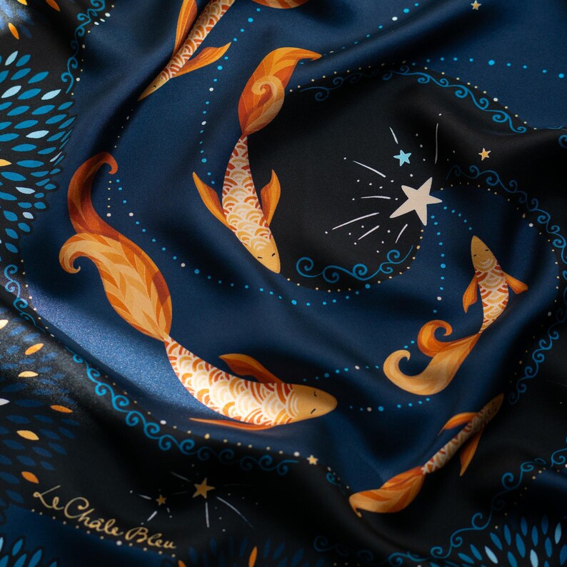 Puede incluir: Un pa&ntilde;uelo de seda azul marino con un dise&ntilde;o celestial. El pa&ntilde;uelo presenta peces koi naranjas estilizados nadando entre estrellas y patrones arremolinados. El texto "Le Ch&acirc;le Bleu" es visible en la esquina inferior izquierda.
