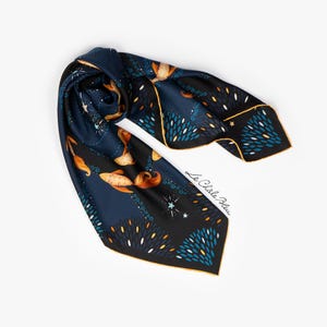 Puede incluir: Pa&ntilde;uelo de seda azul marino con un dise&ntilde;o celestial. El pa&ntilde;uelo presenta detalles dorados, blancos y turquesas, con un borde y el texto "Le Ch&acirc;le Bleu" en blanco. El pa&ntilde;uelo est&aacute; doblado y drapeado.