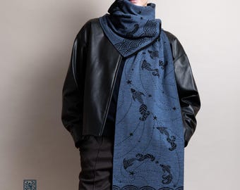 May include: A blue scarf with a black fish and star pattern. The scarf is draped over a black leather jacket. The scarf has a high collar and a rectangular shape with a wave pattern at the bottom.
