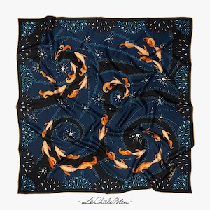 Puede incluir: Pa&ntilde;uelo cuadrado de seda con fondo azul marino que presenta un patr&oacute;n de peces naranjas, estrellas blancas y l&iacute;neas negras en espiral. El borde es negro con detalles azules y blancos. El texto "Le Chale Bleu" est&aacute; en la esquina inferior derecha.