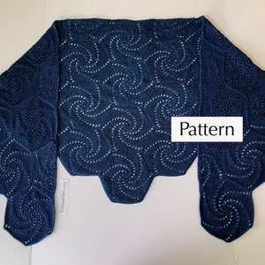 A crochet shawl lies flat on a surface with the two ends folded over. The shawl is made of hexagons with a swirl pattern.