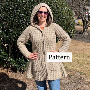 Peut inclure: Un cardigan à capuche en crochet beige avec une fermeture à boutons et des poches. Le cardigan a une ourlet évasé et est porté par une personne avec des lunettes de soleil. Le texte "Pattern" est visible sur un rectangle blanc.