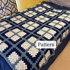 May include: A crocheted blanket with a blue, white, and gray checkered pattern. The blanket is on a bed with a blue headboard and a blue bedspread. The word "Pattern" is written on a white tag attached to the blanket.