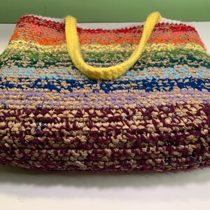 A crochet tote bag lies on its side to show the bottom. It's made from a combination of yarn and plastic yarn made from grocery bags.