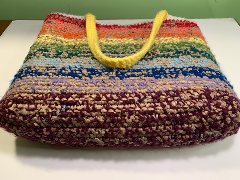 A crochet tote bag lies on its side to show the bottom. It's made from a combination of yarn and plastic yarn made from grocery bags.