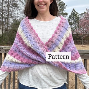 May include: A crocheted shawl with a scalloped edge in shades of pink, purple, and white. The shawl is draped over a person's shoulders. The word "Pattern" is written on the shawl.