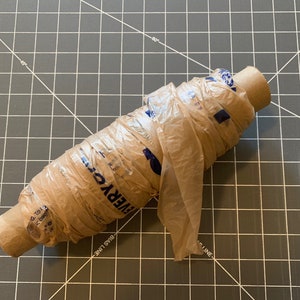 A roll of plastic yarn made from plastic grocery bags sits on a crafting surface.