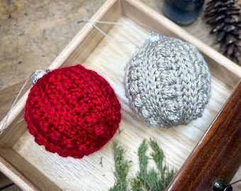 May include: Two crocheted Christmas ornaments in a wooden drawer. One ornament is red and the other is beige.