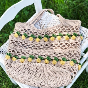 Puede incluir: Una bolsa de mano de crochet con base marr&oacute;n y detalles de pi&ntilde;a amarillos y verdes. La bolsa est&aacute; sentada en una silla blanca.