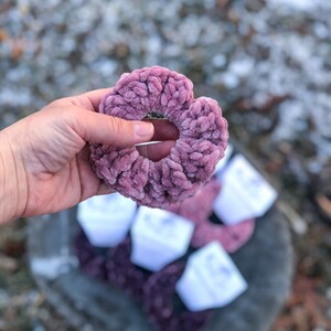 May include: A close-up of a soft, pink, fuzzy hair scrunchie. The scrunchie is made of a thick, textured fabric and is held in a hand.