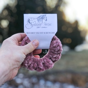 May include: A dusty rose crochet velvet scrunchie with a white tag that reads "Spotted Horse Craft Company" and "Crochet Velvet Scrunchie".