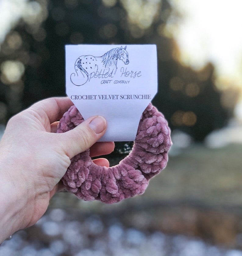 May include: A dusty rose crochet velvet scrunchie with a white tag that reads "Spotted Horse Craft Company" and "Crochet Velvet Scrunchie".