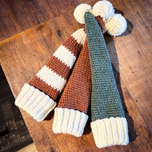 Puede incluir: Tres gorros de punto con pompones. Un gorro es de rayas marrones y blancas, otro es marr&oacute;n y el &uacute;ltimo es verde.