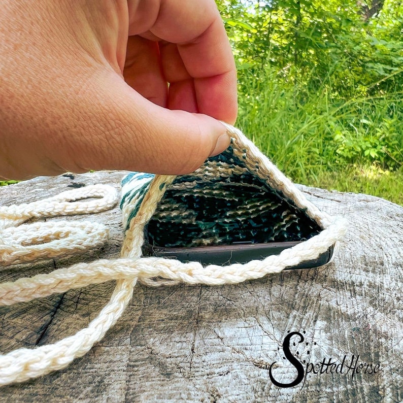Puede incluir: Primer plano de una funda para tel&eacute;fono hecha de fibras naturales tejidas. La funda est&aacute; abierta y se ve un tel&eacute;fono en su interior. La funda es de color verde claro y blanco con una textura de fibra natural.