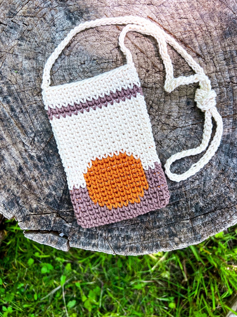 May include: A crocheted beige, brown, and orange crossbody bag with a long strap. The bag has a geometric design with a circle in the center.