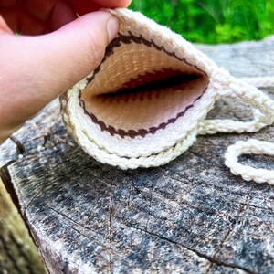 May include: A small, white crocheted pouch with a brown and white geometric pattern. The pouch is open and the inside is visible.
