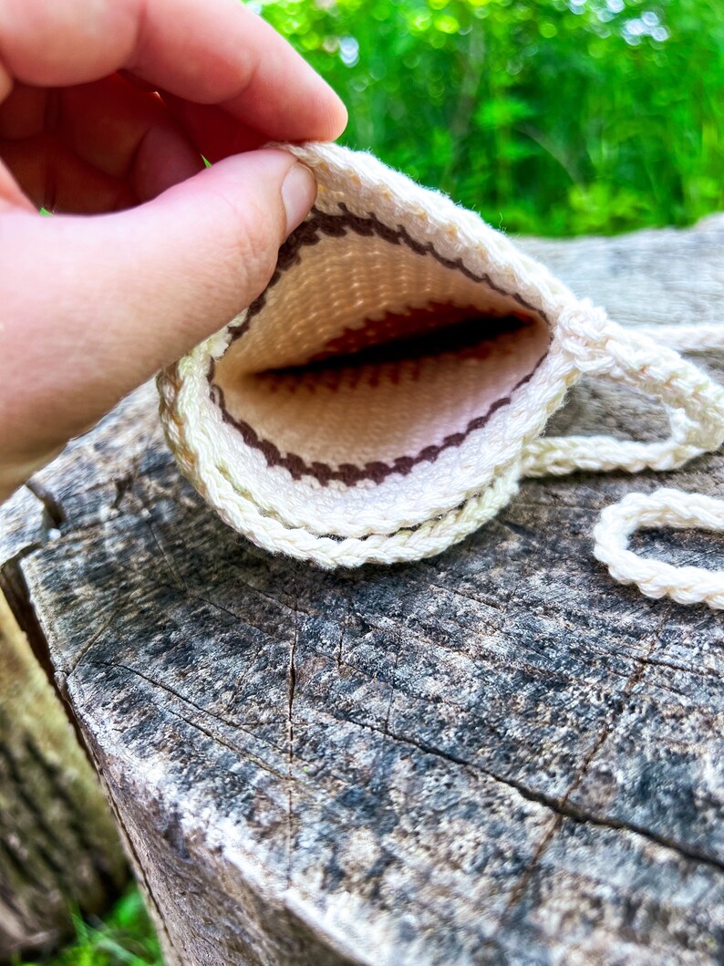 May include: A small, white crocheted pouch with a brown and white geometric pattern. The pouch is open and the inside is visible.