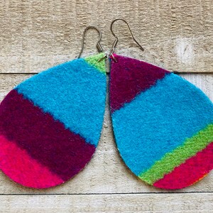 May include: A pair of teardrop-shaped earrings with a colorful striped pattern. The earrings are made of felt and have silver hooks. The colors of the stripes are pink, purple, blue, and green.
