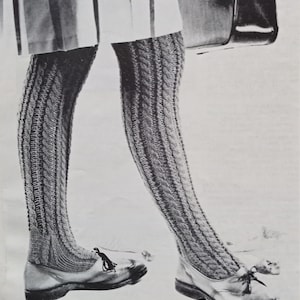 May include: A pair of gray knitted leg warmers with a cable knit pattern. The leg warmers are worn with black shoes.