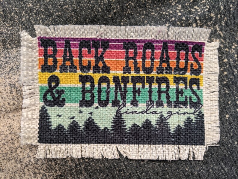 Może przedstawiać: Biała łatka z tkaniny z kolorowym wzorem w paski tęczy i tekstem "Back Roads & Bonfires kinda girl".