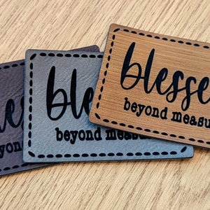 May include: Three rectangular plaques with the word "blessed" in a script font, and "beyond measure" in a smaller font. The plaques are in shades of brown, gray, and wood grain, with a stitched border.