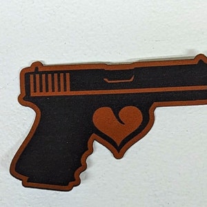 May include: A brown leather patch with a black silhouette of a handgun with a brown heart in the center.