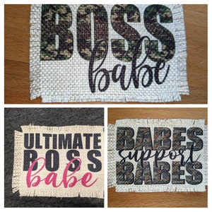 May include: Three burlap patches with text printed on them. The first patch says "BOSS babe" in black text with a camouflage pattern behind the letters. The second patch says "ULTIMATE BOSS babe" in black and pink text. The third patch says "BABES support BABES" in black text with a camouflage pattern behind the letters.