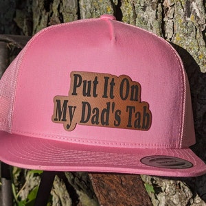 May include: Pink trucker hat with a brown leather patch that says "Put It On My Dad's Tab".