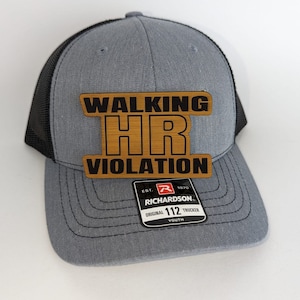 May include: A gray and black youth trucker hat with a brown patch that reads "Walking HR Violation". The hat is made by Richardson and has a black mesh back.