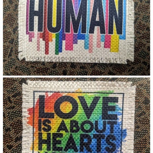 May include: Two fabric patches with rainbow designs and black text. The first patch says "HUMAN" in black letters. The second patch says "LOVE IS ABOUT HEARTS NOT PARTS".