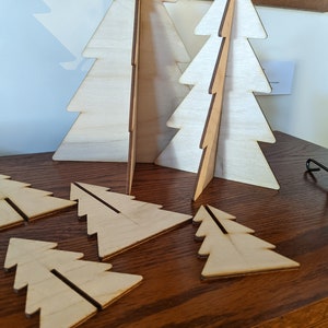May include: A set of wooden Christmas tree ornaments in various sizes. The ornaments are made of light brown wood and have a simple, minimalist design.