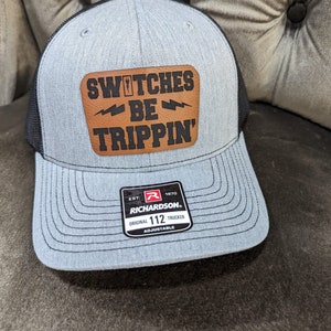 May include: A gray and black trucker hat with a brown leather patch that says "Switches Be Trippin'" and a black and red label that says "Richardson 112 Original Trucker Adjustable".