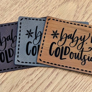 May include: Three wooden signs with a black snowflake and the text "Baby it's cold outside" in black cursive lettering. The signs are brown, gray, and wood.