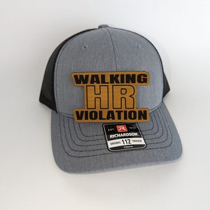 May include: A gray and black mesh trucker hat with a brown patch that says "Walking HR Violation". The hat is a youth size and has the Richardson logo on the back.