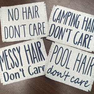 May include: Four white fabric patches with black text. The patches read "No Hair Don't Care", "Camping Hair Don't Care", "Messy Hair Don't Care", and "Pool Hair Don't Care".