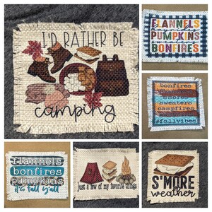 May include: Six burlap patches with fall-themed text and illustrations. The patches include "I'd rather be camping" with a campfire, boots, and a backpack, "Flannels, bonfires, pumpkins, it's fall y'all", "Just a few of my favorite things" with a tent, campfire, and s'mores, "S'more weather", "Bonfires, flannels, smores, sweaters, campfires, #fallvibes", and "Flannels, hayrides, pumpkins, bonfires".