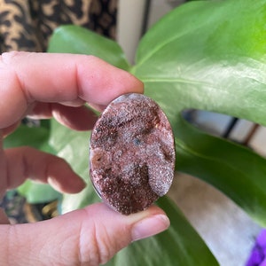 May include: A close-up of a brown and white agate stone with a rough, textured surface. The stone is oval-shaped and has a natural, organic look.