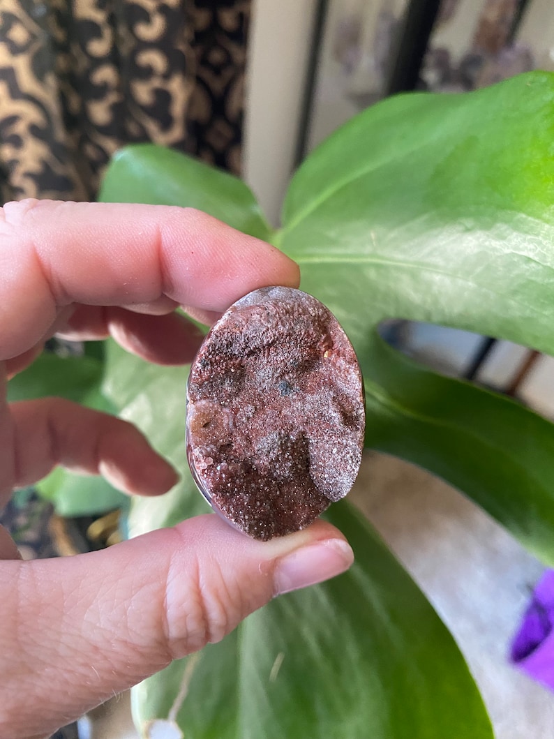 May include: A close-up of a brown and white agate stone with a rough, textured surface. The stone is oval-shaped and has a natural, organic look.