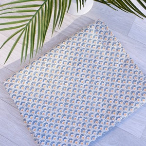 Pode incluir: Um tecido estampado azul e amarelo com um design geométrico. O tecido tem um fundo branco com círculos azuis e amarelos dispostos em um padrão repetitivo.