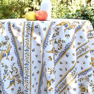 Könnte beinhalten: Eine weiße Tischdecke mit einem blauen und gelben Blumenmuster mit Vögeln. Die Tischdecke liegt auf einem runden Tisch mit drei Äpfeln und einer weißen Flasche darauf.