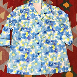 May include: A button-down shirt with a floral pattern. The shirt features a white background with blue and light blue flowers and green accents. The sleeves are three-quarter length.