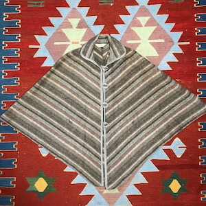 Puede incluir: Un poncho de rayas marrones y grises con cuello blanco y cierre de botones.