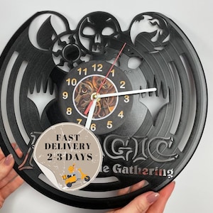 May include: Black vinyl record clock featuring a Magic: The Gathering logo with a skull and wings design. The clock face has a detailed design with Roman numerals and a red second hand.