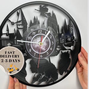 May include: Black vinyl record clock featuring a silhouette of Hogwarts castle and other Harry Potter themed imagery. The clock face has black Roman numerals and white hands. The clock is 12 inches in diameter.