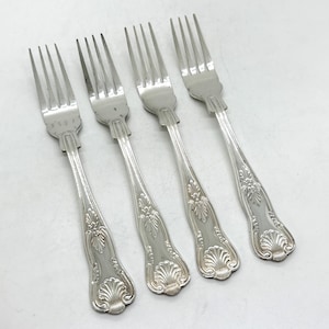 Peut inclure: Quatre fourchettes argentées avec des motifs floraux et coquillages ornés sur les manches. Les dents sont espacées uniformément. Les fourchettes sont disposées en diagonale sur une surface blanche.