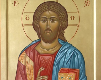 May include: A religious icon depicting Jesus Christ with a blue robe and red undergarment. He is holding a book in his left hand and has a halo above his head. The icon is painted on a gold background with the Greek letters "IC XC" in the corners.