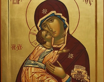 May include: A religious icon depicting the Virgin Mary holding the baby Jesus. The icon is painted on a wooden panel with gold leaf accents. The Virgin Mary is wearing a red robe with gold trim and a blue sash. The baby Jesus is wearing a white robe with gold trim. The icon is framed in a gold frame.
