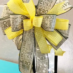 May include: A black lantern with a yellow and white ribbon bow. The ribbon has the words "Freedom, Duty, USA, Defend, Hero" printed on it.